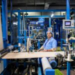 Smiling female textile worker operating machinery in a modern factory environment.
